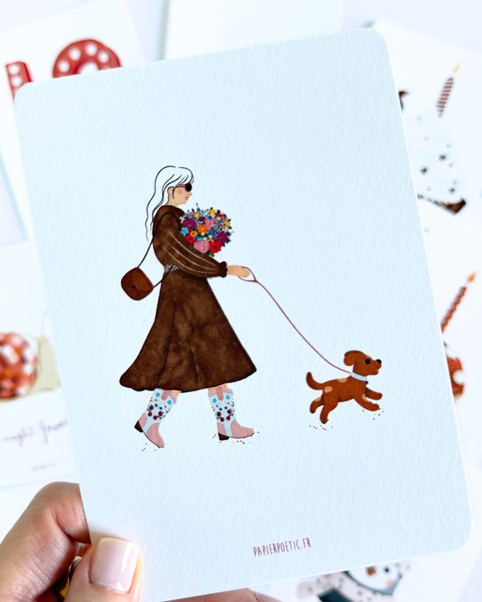 A minimalist watercolor art print featuring a woman in a brown coat walking a small brown dog while holding a colorful bouquet of flowers. The print is presented on a white card with a subtle drop shadow against a white background.