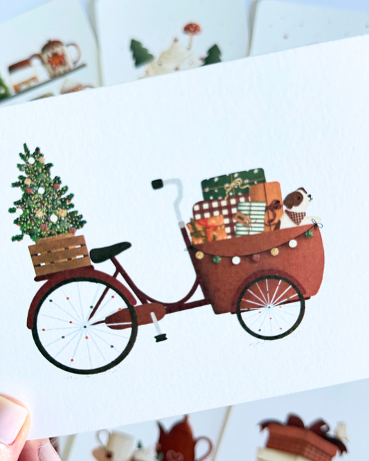 A whimsical illustration of a brown cargo bicycle carrying a decorated Christmas tree, wrapped gifts, and a small dog, shown on a white background with a thin gray border.