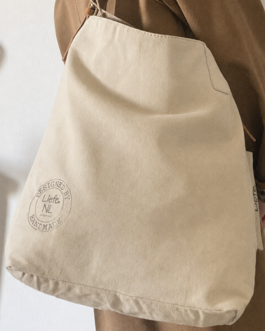 A beige canvas shoulder bag with a brown leather strap and a circular 'Life is Beautiful' logo printed on the front, displayed against a white background.
