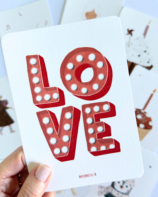 A vertical art print featuring the word 'LOVE' in large, 3D marquee-style letters with white light bulbs, printed in coral red on a white background. Small text at the bottom reads 'PARIHOEOTIC.