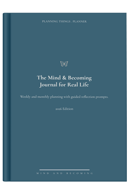 Blue journal titled 'The Mind & Becoming Journal for Real Life' on a light surface with a decorative item.