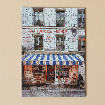 Jigsaw puzzle of a café scene with 'Au Tour de France' sign on a beige background