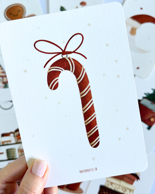 A vertical rectangular print or card featuring a stylized brown candy cane with white stripes and a brown bow, centered on a white background with faint small star motifs. The text 'PAPIERMOYEC.