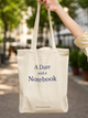 Tote bag with 'A Date with a Notebook' text held by a person outdoors.