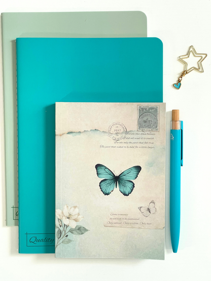 Teal notebook with butterfly design, pen, and decorative star charm on a white background