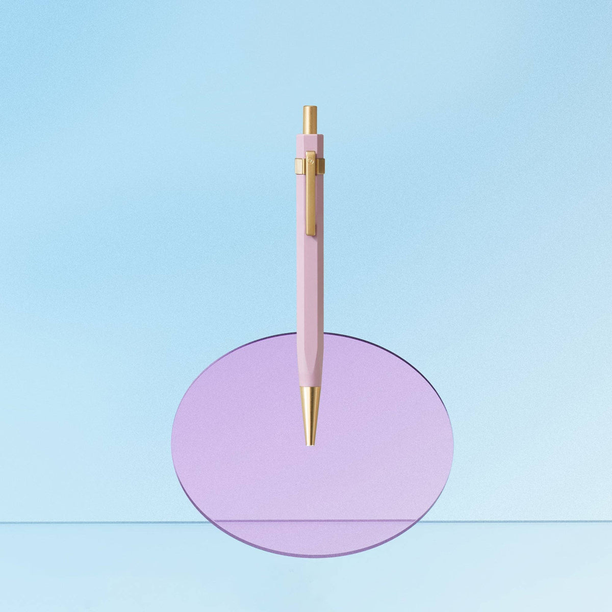 Pink pen with gold accents on a purple circular stand against a light blue background