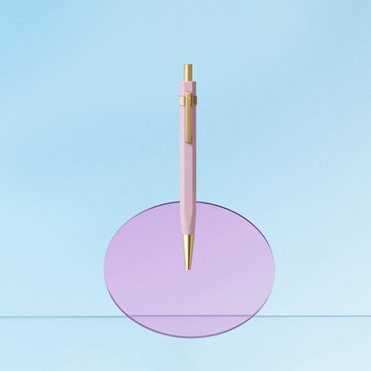 Pink pen with gold accents on a purple circular stand against a light blue background
