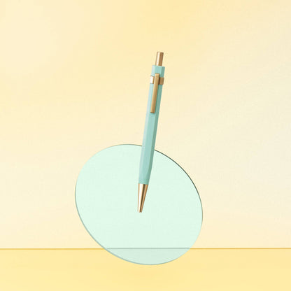 Light blue pen with gold accents on a light green circular stand against a yellow background
