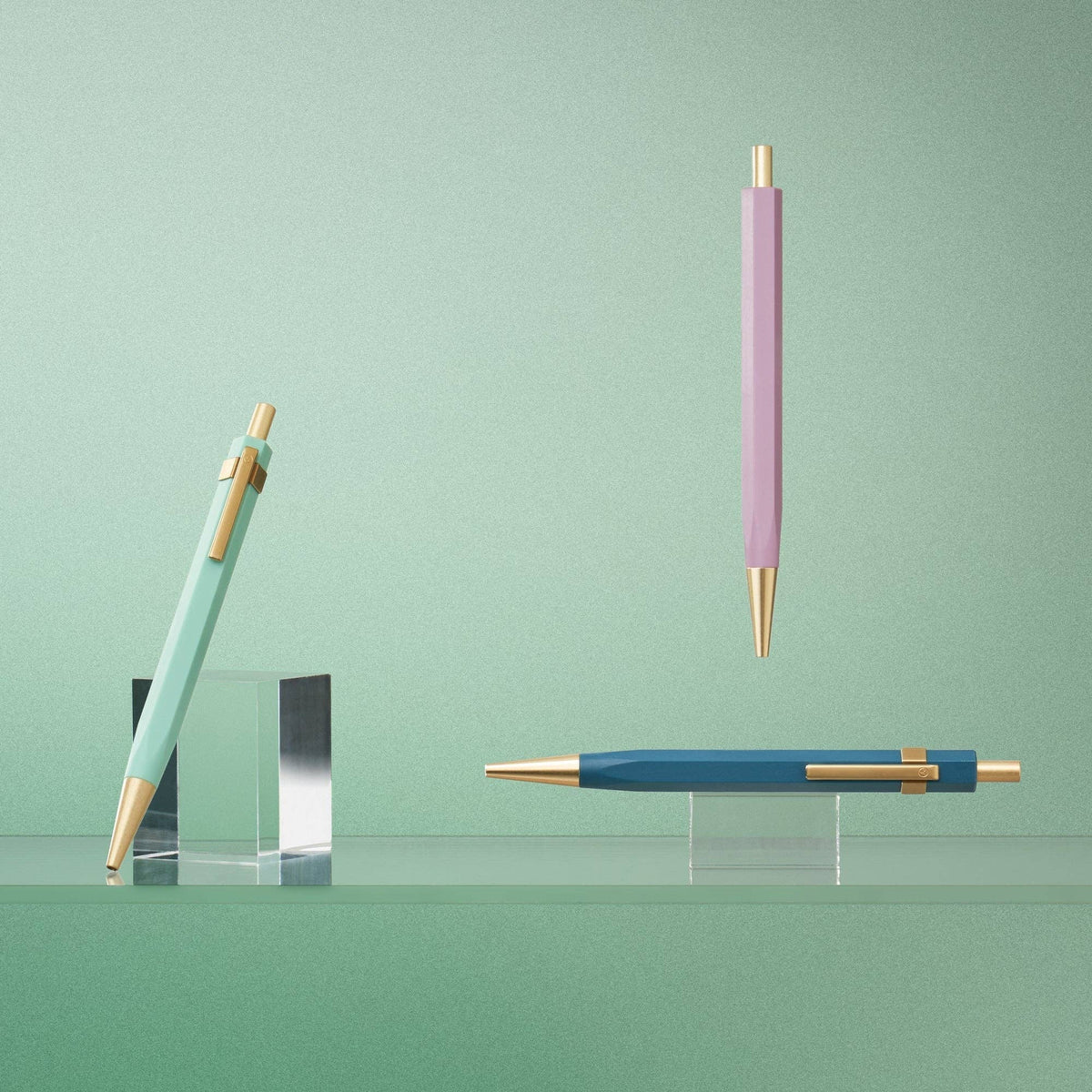 Three pens with different colored bodies and gold accents on a light green background