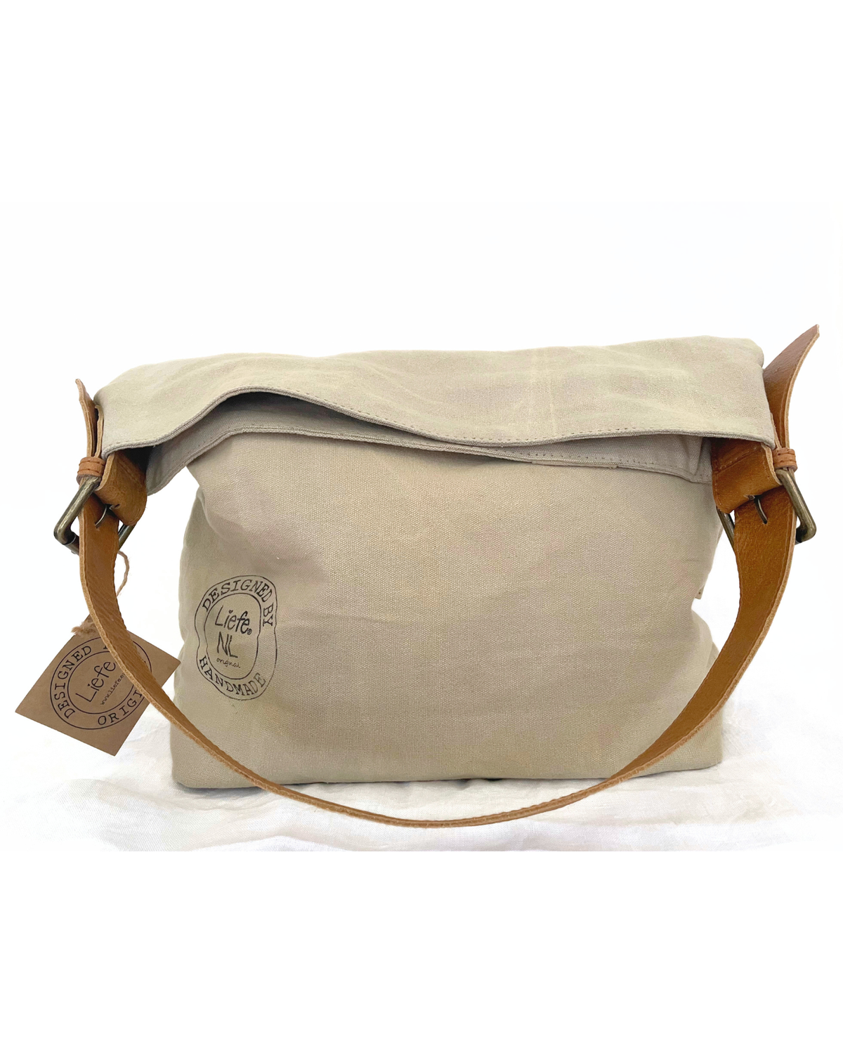 A beige canvas messenger bag with a brown leather strap and buckle, featuring a circular embossed logo on the front and a hanging paper tag.