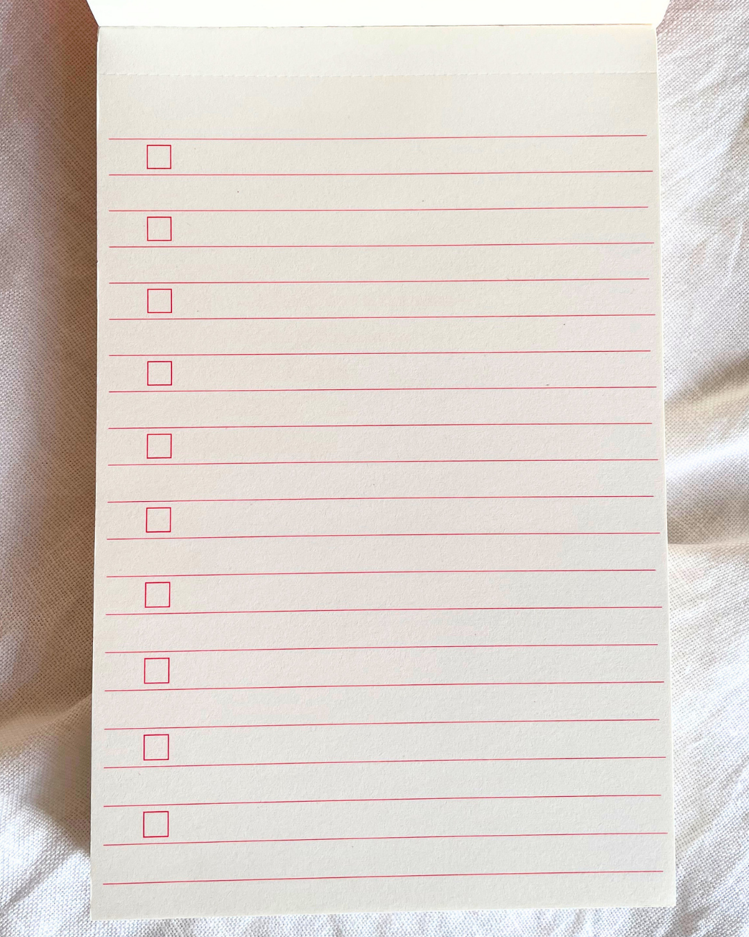 Notebook page with red lines and checkboxes on a textured surface