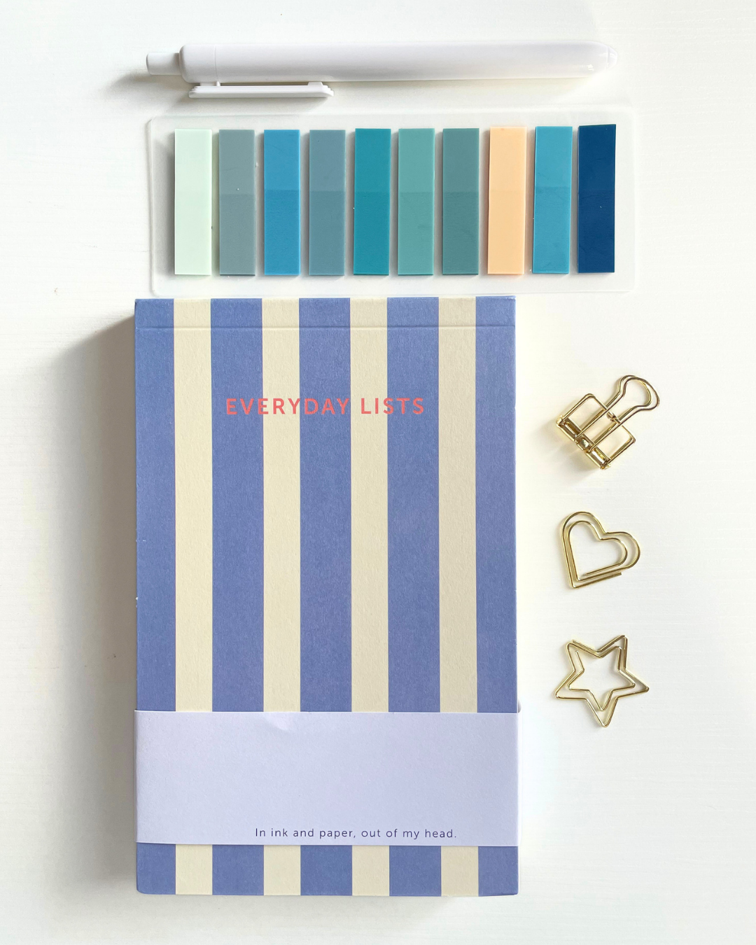 Notebook with blue and beige striped cover titled 'Everyday Lists' on a beige fabric background.