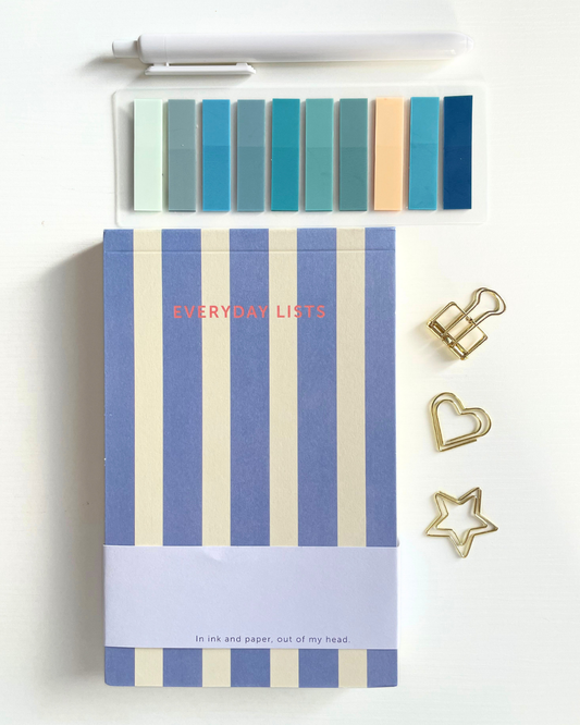 Notebook with blue and beige striped cover titled 'Everyday Lists' on a beige fabric background.