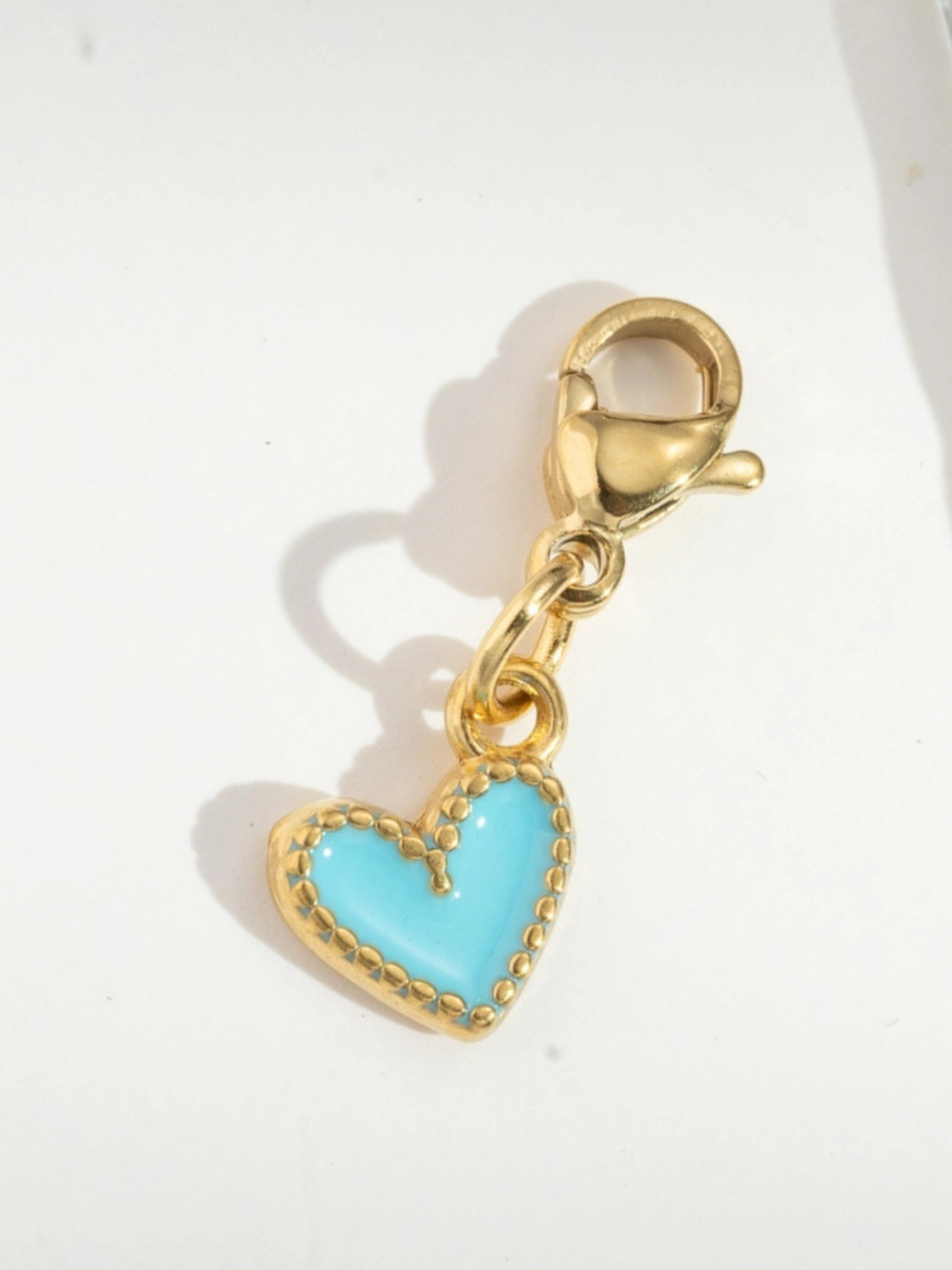 Gold charm with a turquoise heart on a white background