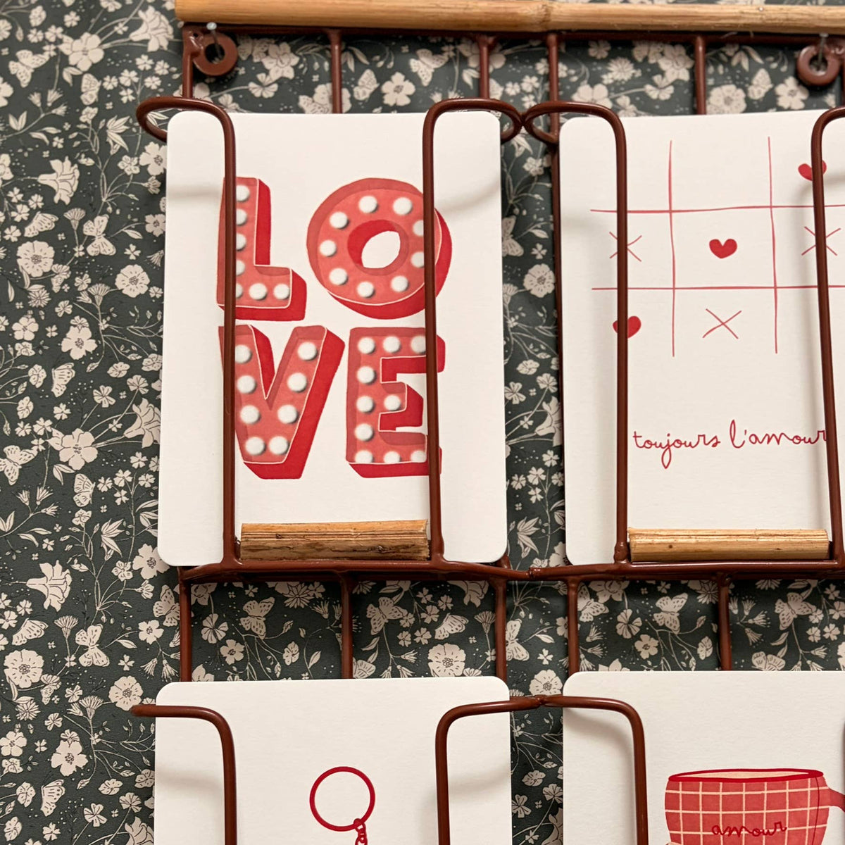 Set of tea towels with decorative designs on a floral-patterned wall.