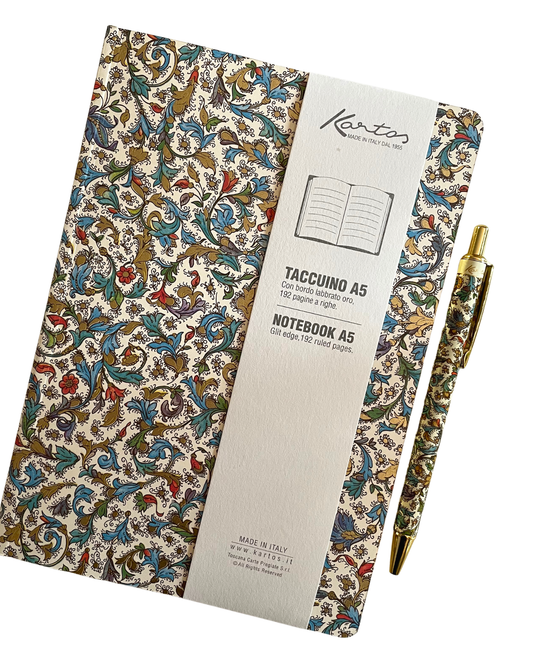 A Kento notebook with an ornate multicolor floral and scroll pattern on a cream background, shown with a white paper sleeve and a matching gold pen on a clean white background.