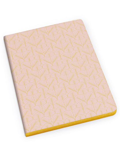 A rectangular notebook with a pale pink cover featuring a repeating gold geometric pattern, shown at an angle on a solid white background.