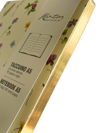 Kantos A5 notebook with a cream-colored cover decorated with delicate floral illustrations and a metallic gold edge, shown at an angle on a white background.