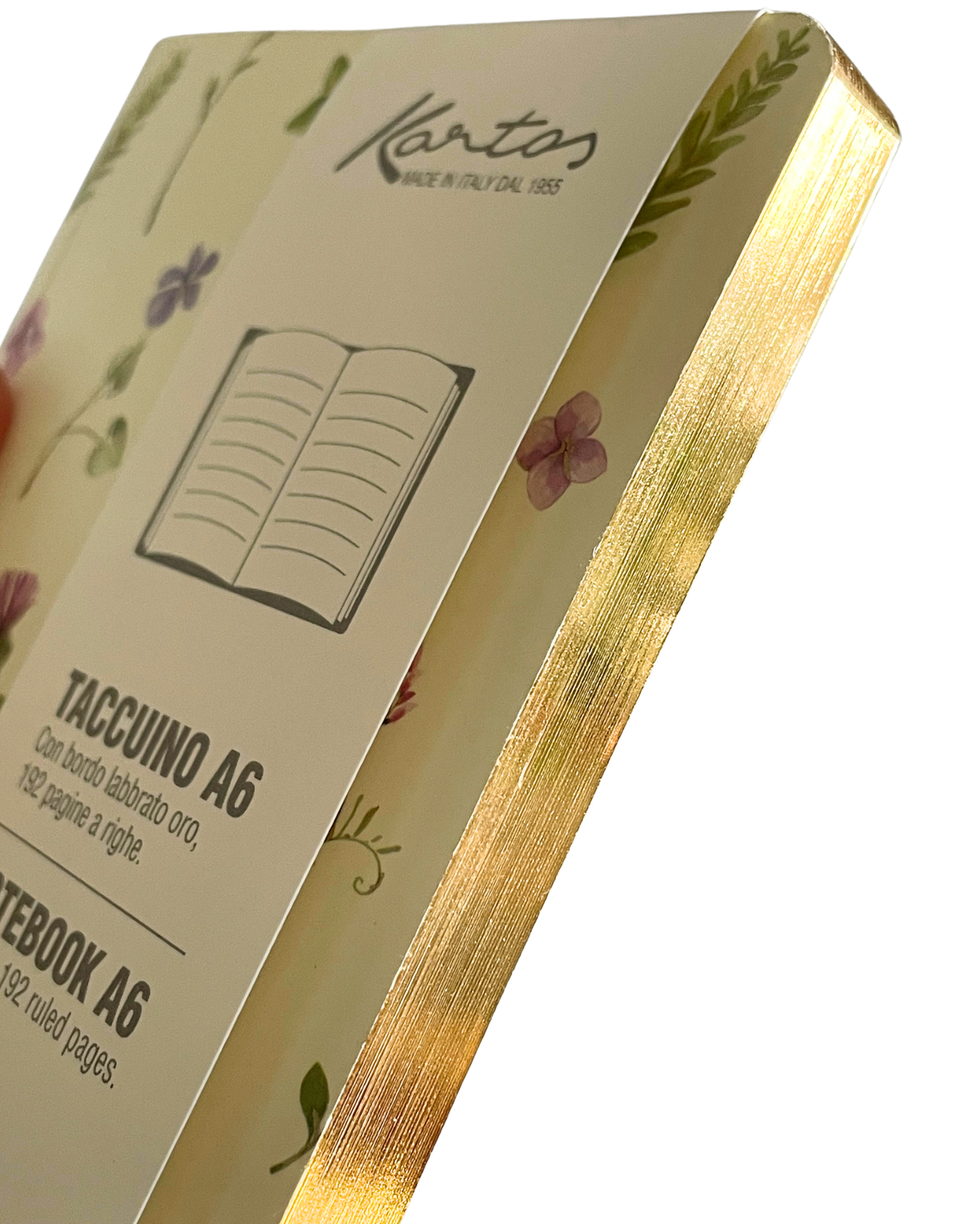A close-up of a Kantos A6 notebook showing the cream-colored cover with delicate floral illustrations, gold foil edges, and printed text including 'TACCUINO A6' and 'NOTEBOOK A6'.