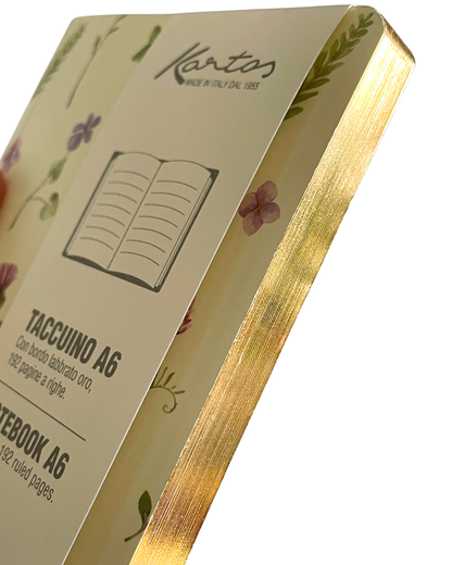 A close-up of a Kantos A6 notebook showing the cream-colored cover with delicate floral illustrations, gold foil edges, and printed text including 'TACCUINO A6' and 'NOTEBOOK A6'.