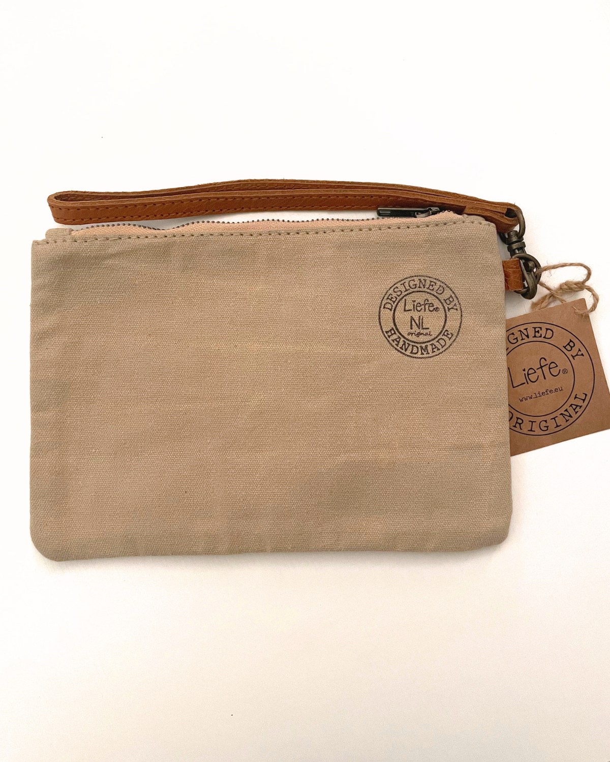 A small beige canvas wristlet pouch with a brown leather wrist strap and zipper, featuring a circular embossed 'Liefte' logo on the front and a matching brown paper hangtag.