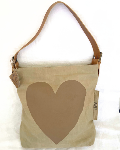 A beige canvas shoulder bag with a large brown heart on the front and a tan leather strap, shown against a white background.