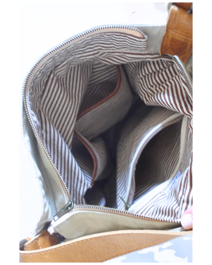 Close-up of the interior of a handbag, showing a striped fabric lining in beige and brown tones, with a tan leather strap visible at the top and bottom edges.