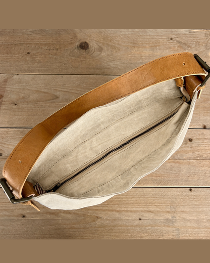 A top-down view of a tan leather belt bag with a beige canvas interior, displayed on a rustic wooden plank surface.