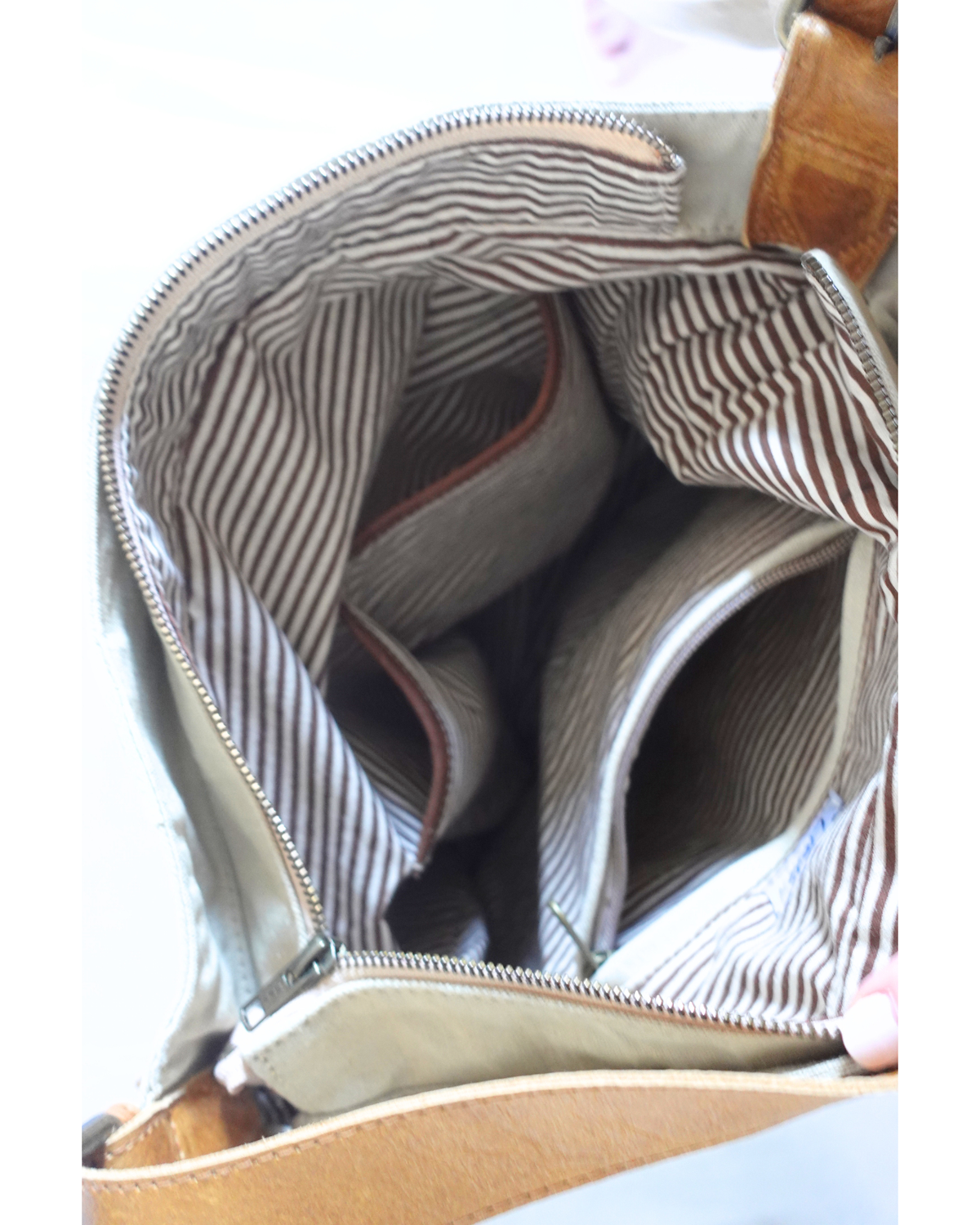 An off-white canvas tote bag with brown leather handles, hanging against a white wall next to a brown coat. The bag features a circular 'Lief & Leben' logo on the front and a side tag.