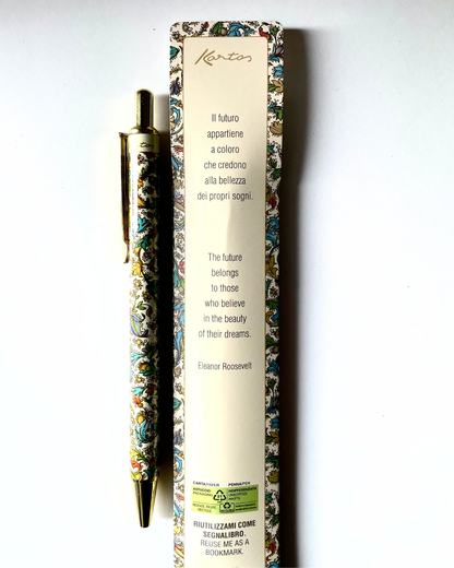 Una penna dorata decorativa con fusto decorato con motivi colorati è esposta accanto alla sua alta scatola color crema su uno sfondo bianco uniforme. La scatola presenta un testo in italiano e in inglese e una citazione di Eleanor Roosevelt.
