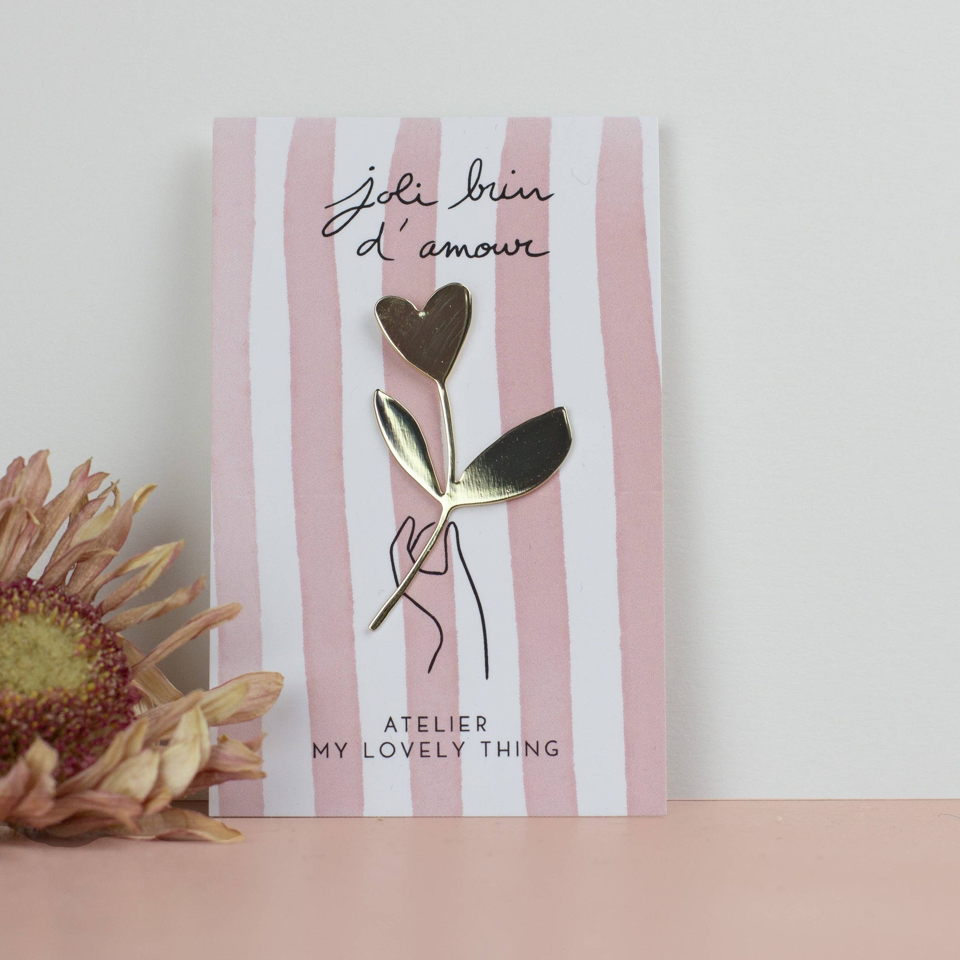 Gold and silver heart-shaped brooch on a striped card with floral decoration.