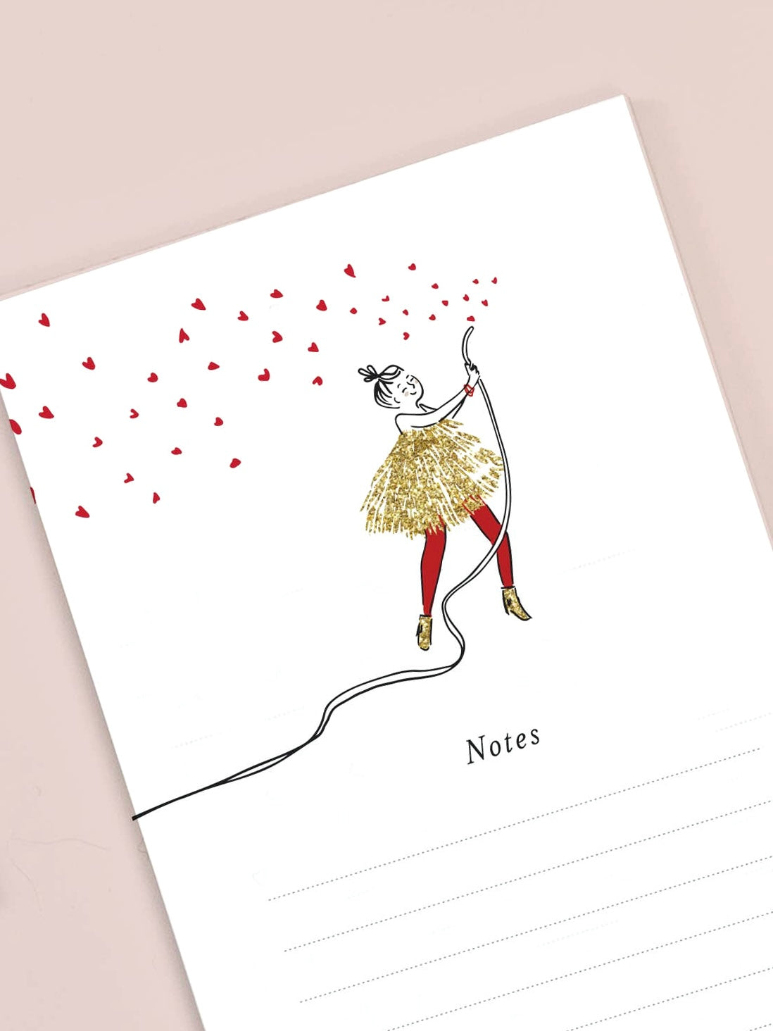 Notebook with a decorative design of a girl in a gold dress and red shoes holding a string of hearts, on a beige background.