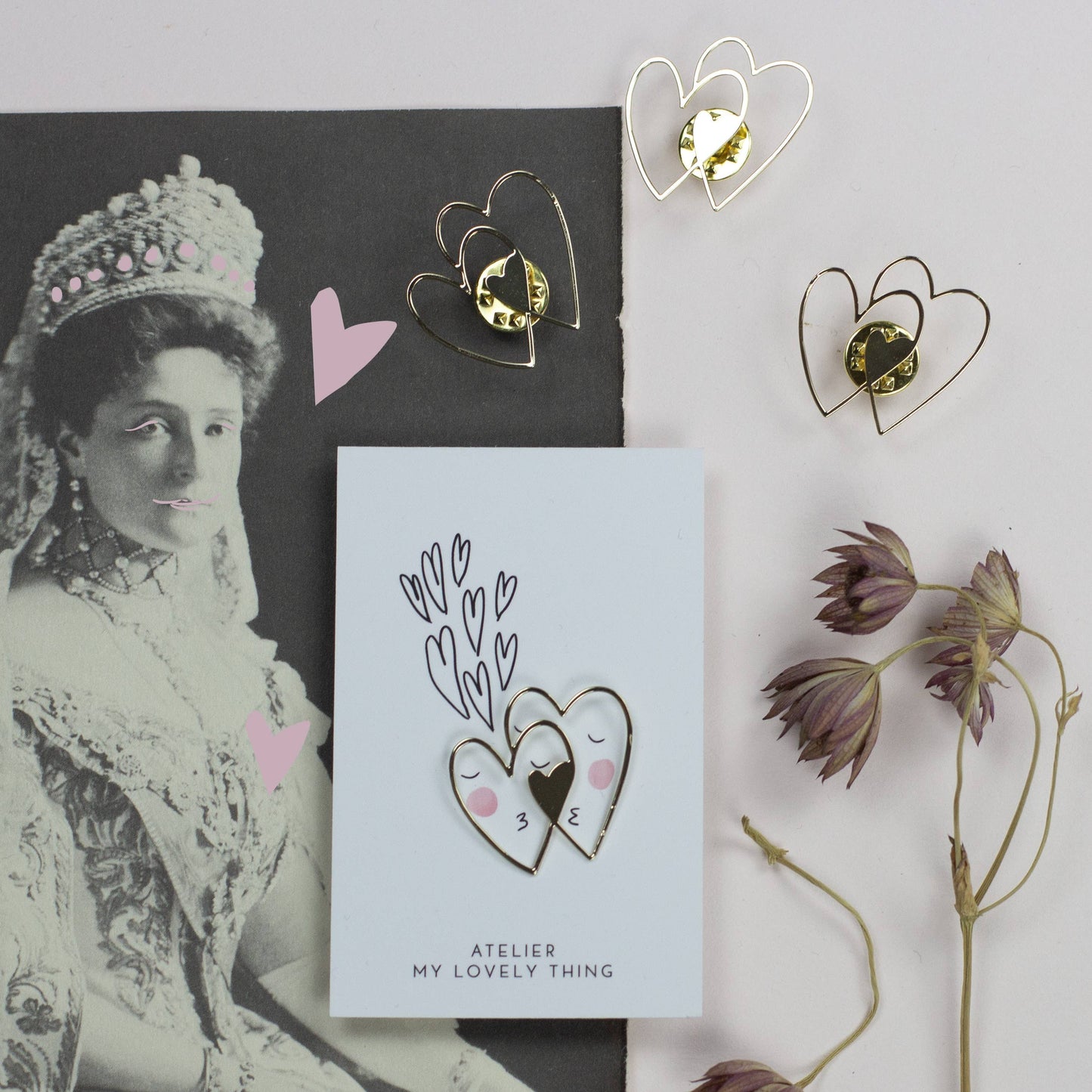 Heart-shaped earrings on a card with a vintage portrait and dried flowers.