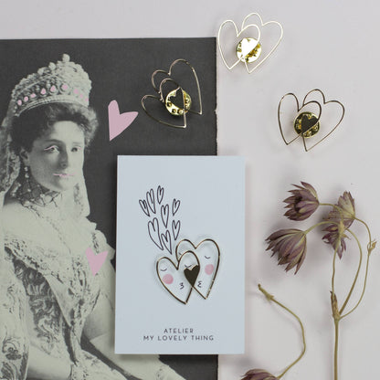 Heart-shaped earrings on a card with a vintage portrait and dried flowers.