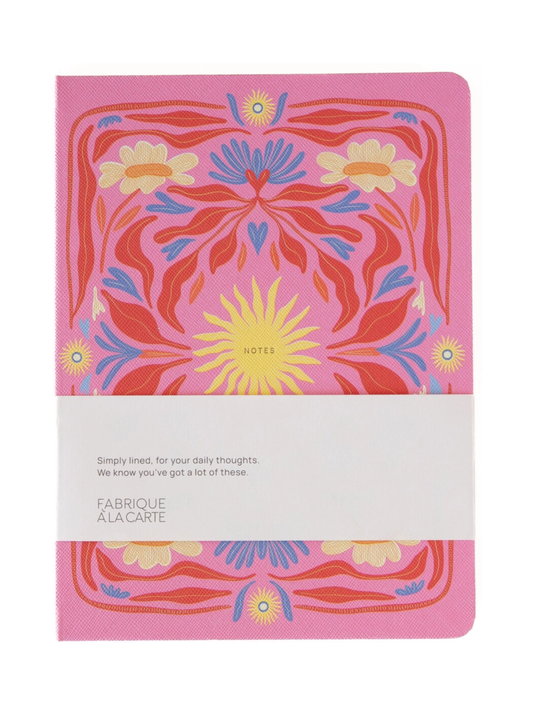 A pink Fabrique & La Carte notebook with a colorful floral pattern on the cover, wrapped in a white paper band.