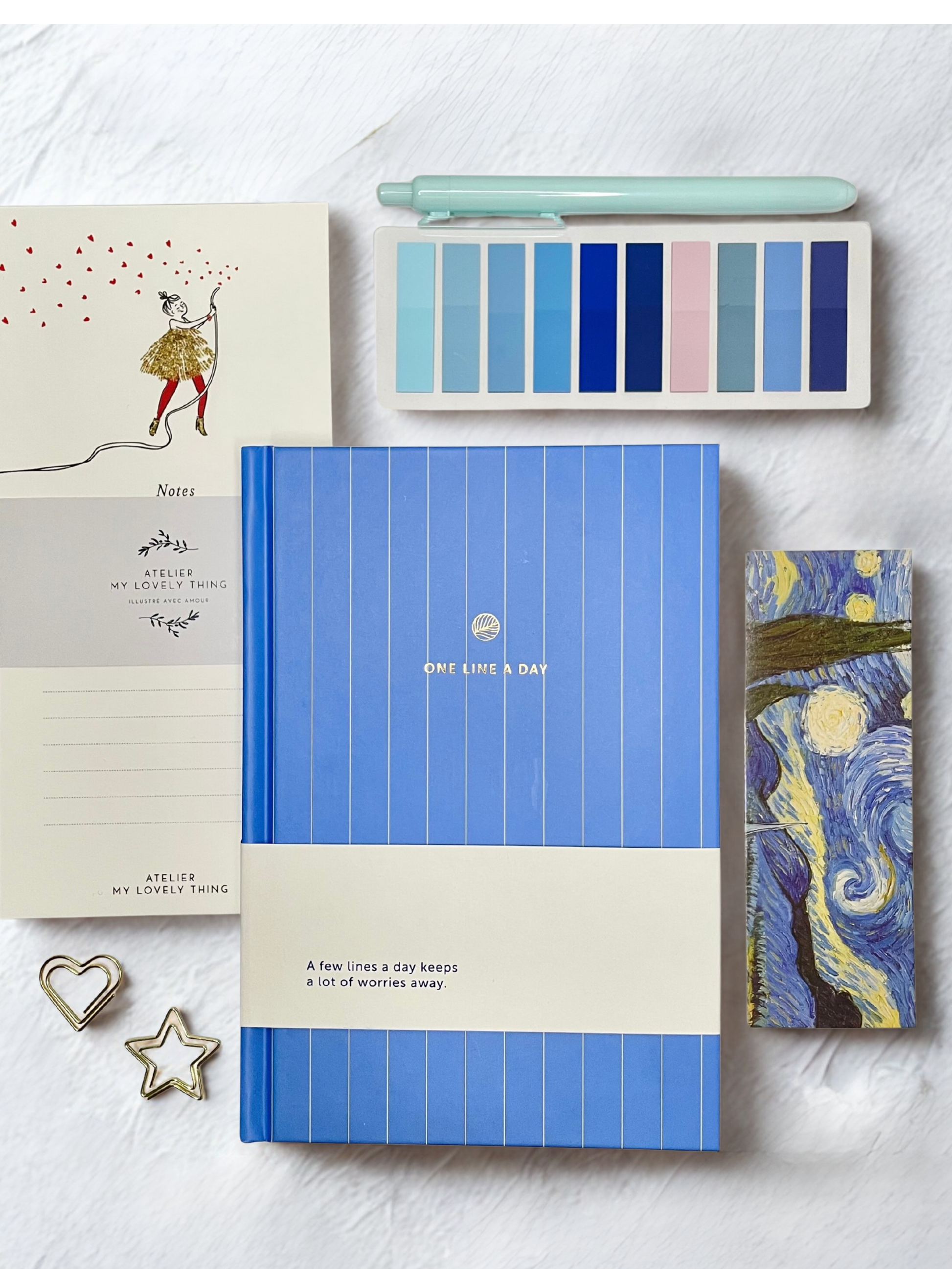 Blue notebook with a cream band, surrounded by stationery items on a light gray background
