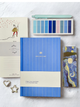 Blue notebook with a cream band, surrounded by stationery items on a light gray background