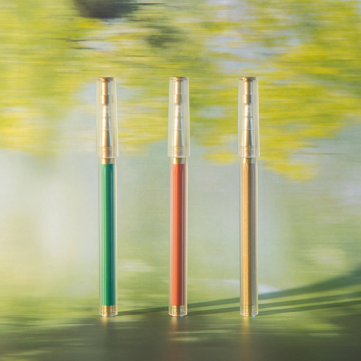 Three pens with green, red, and gold accents on a blurred natural background