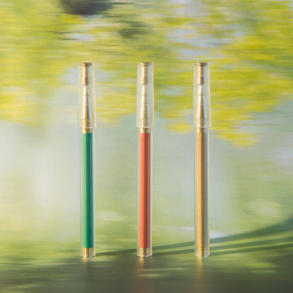 Three pens with green, red, and gold accents on a blurred natural background