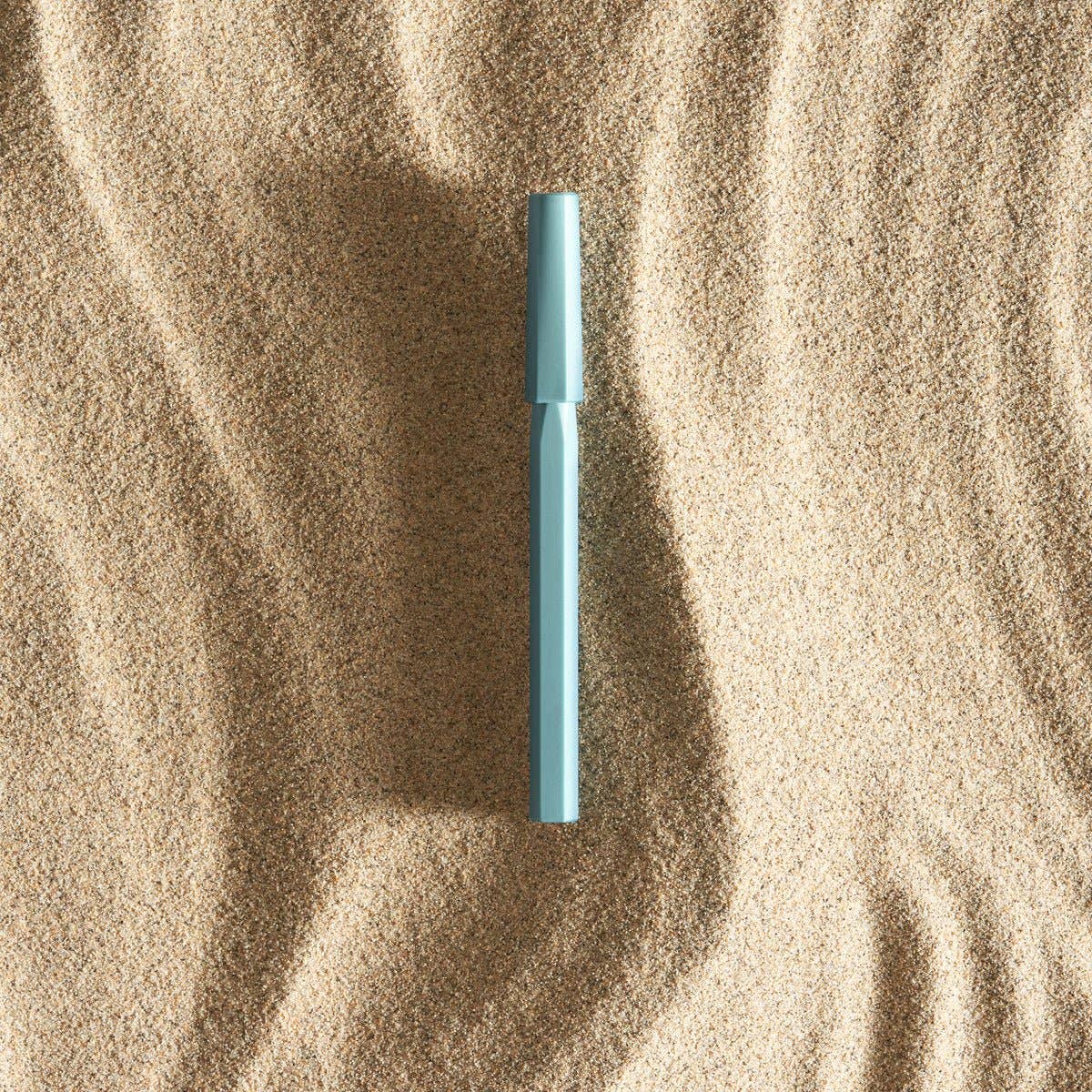 Blue pen lying on sand with a shadow