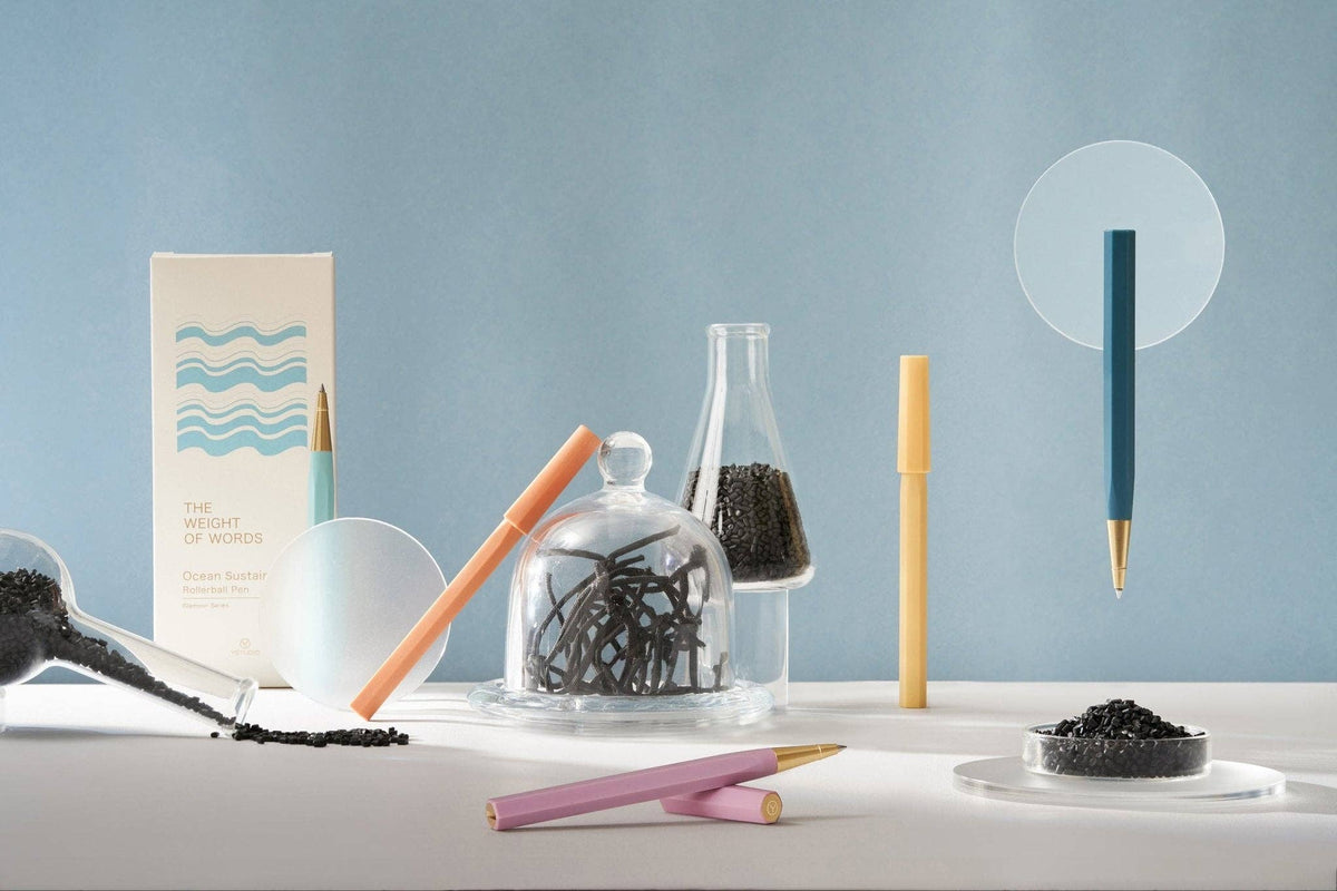 Stationery items including pens, a jar of pins, and small containers on a light blue background.