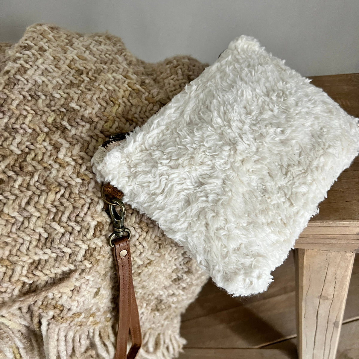 White fluffy pouch with a brown strap on a textured surface