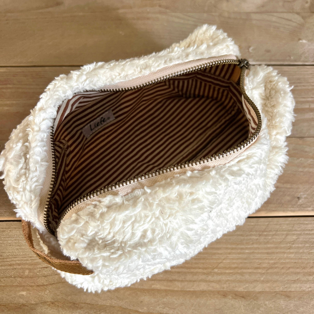 Fluffy white pouch with a zipper on a wooden surface