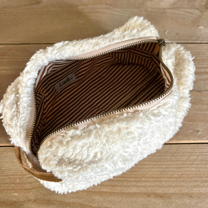 Fluffy white pouch with a zipper on a wooden surface
