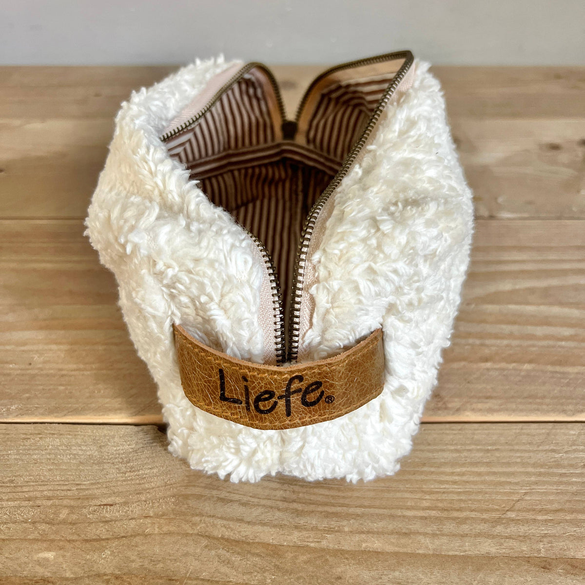 A white sherpa zippered pouch with a brown faux-leather strap featuring the embroidered brand name 'Liefe'.