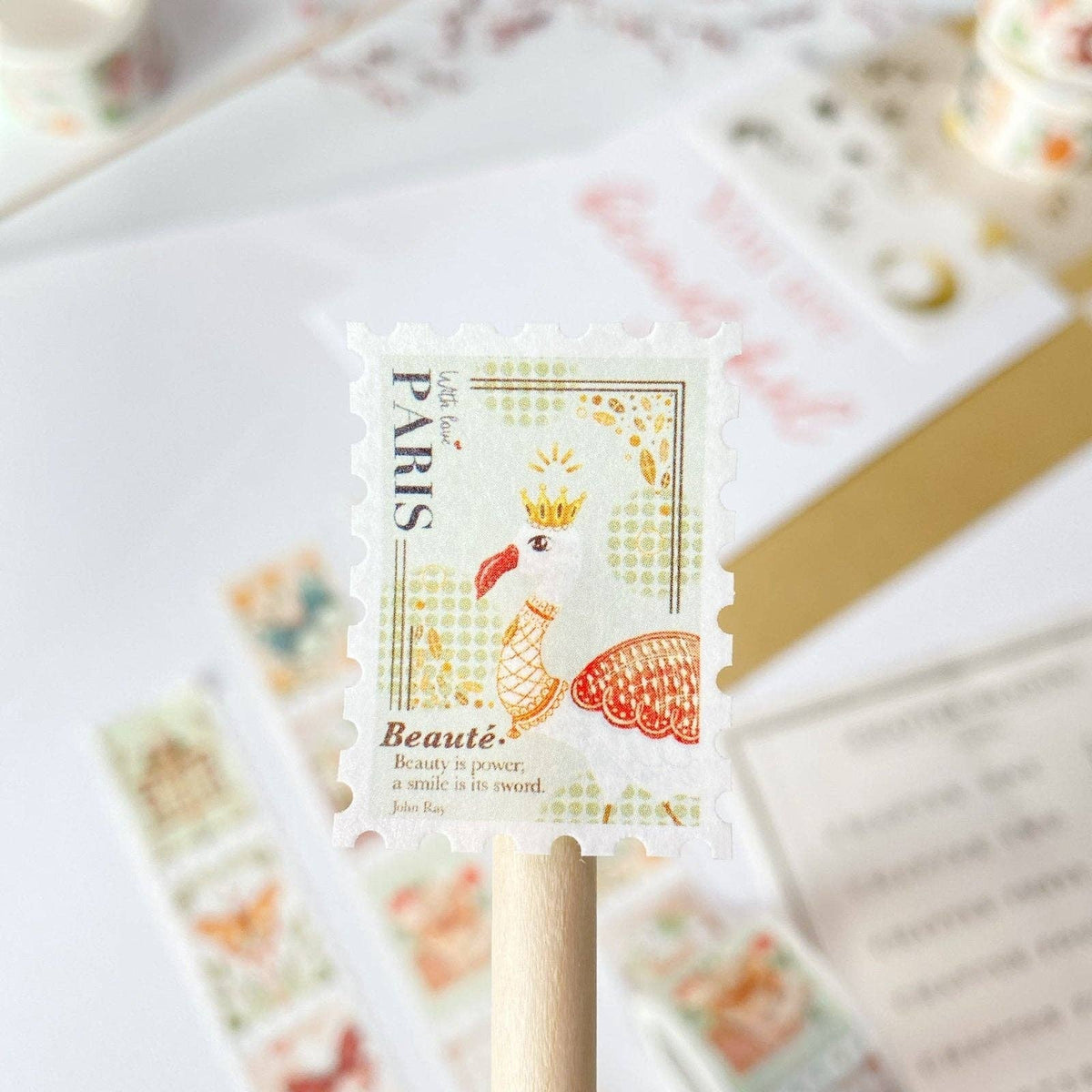A decorative Paris postage stamp design on a wooden stick, with a blurred background of matching stationery and envelopes.