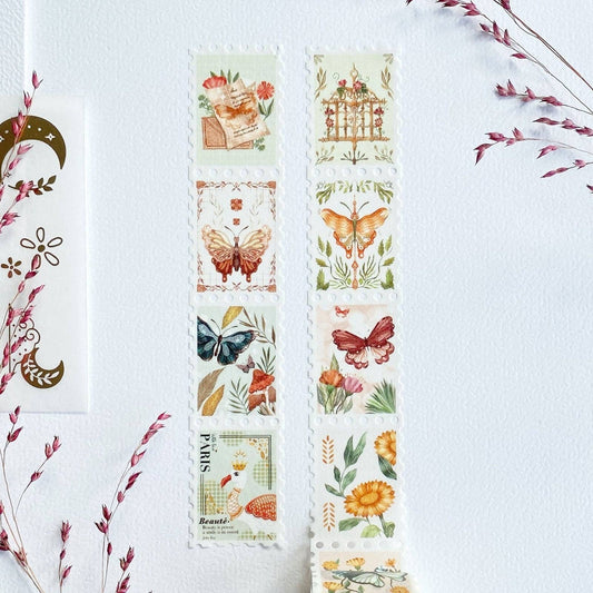 Two vertical strips of decorative washi tape with vintage-style illustrated stamps, displayed on a white textured background with dried floral accents.