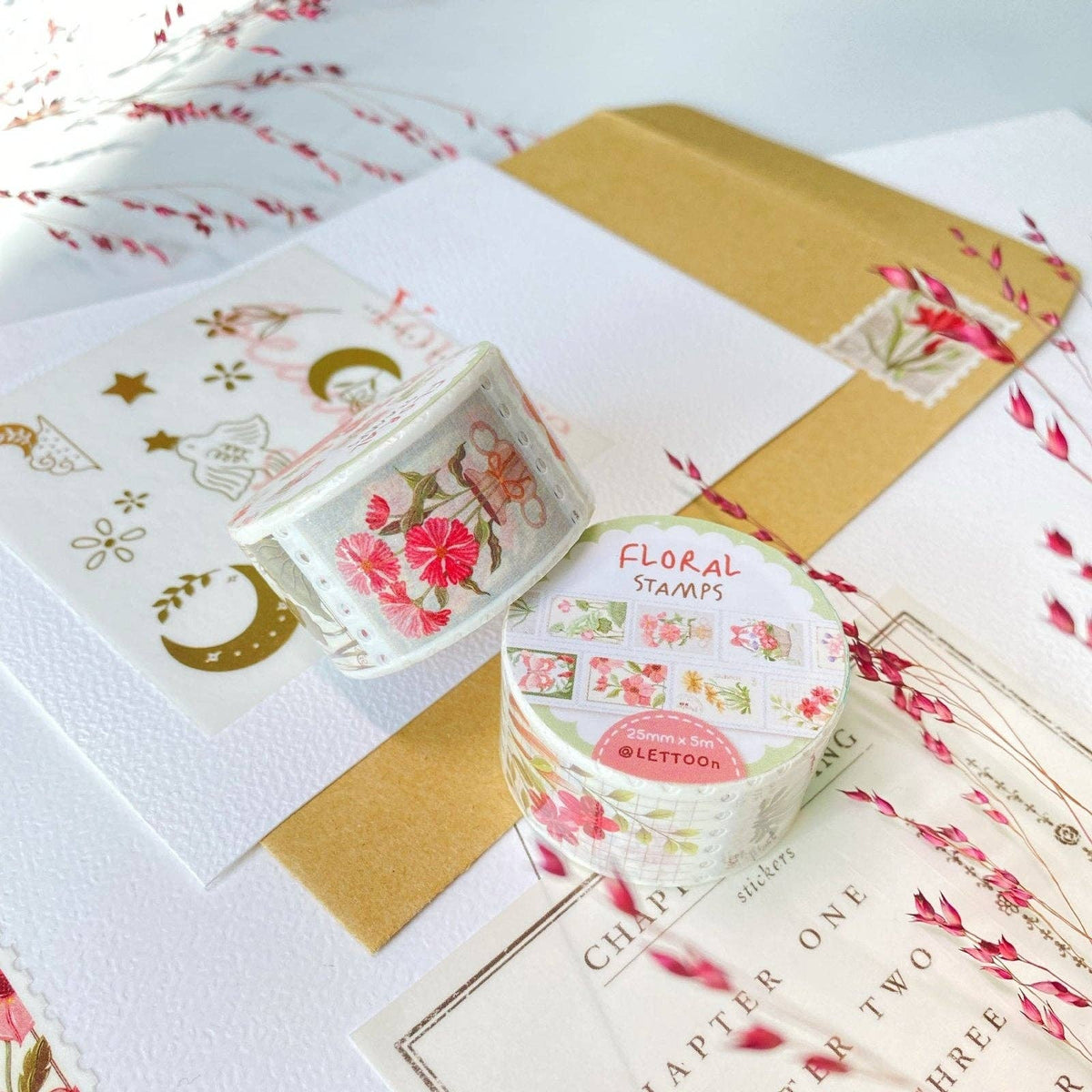 Floral stamps in a container on a white surface with decorative paper and envelopes.