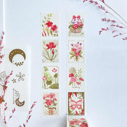 A set of floral washi tapes arranged on a textured white background, alongside a sheet of decorative washi tapes featuring a gold crescent moon and floral motifs, accented by dried pink flowers in the corners.