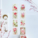 A set of floral washi tapes arranged on a textured white background, alongside a sheet of decorative washi tapes featuring a gold crescent moon and floral motifs, accented by dried pink flowers in the corners.